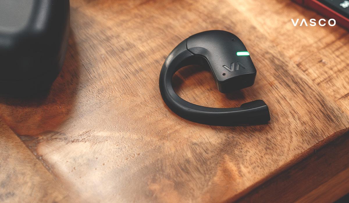 Detailní záběr na sluchátko Vasco Translator na dřevěném stole s LED kontrolkou