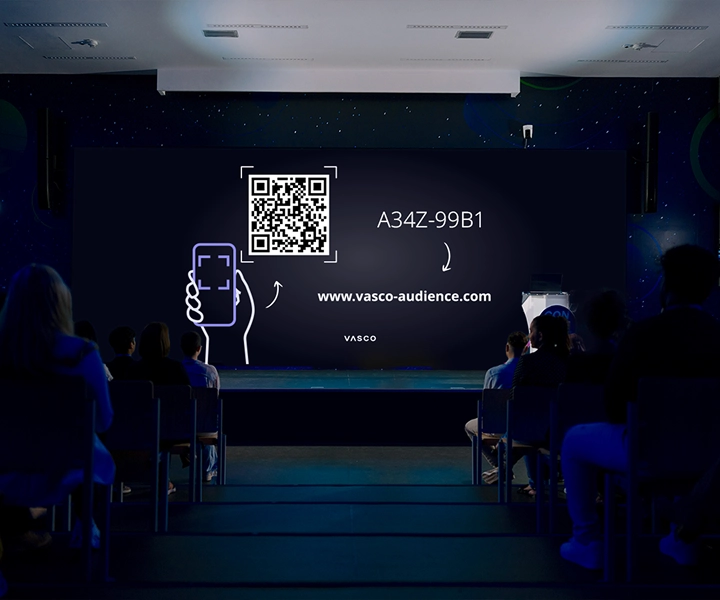 Na velké obrazovce v konferenční místnosti se zobrazují pokyny „Připojte se k Vasco Audience“, které účastníkům ukazují, jak se připojit k relaci.